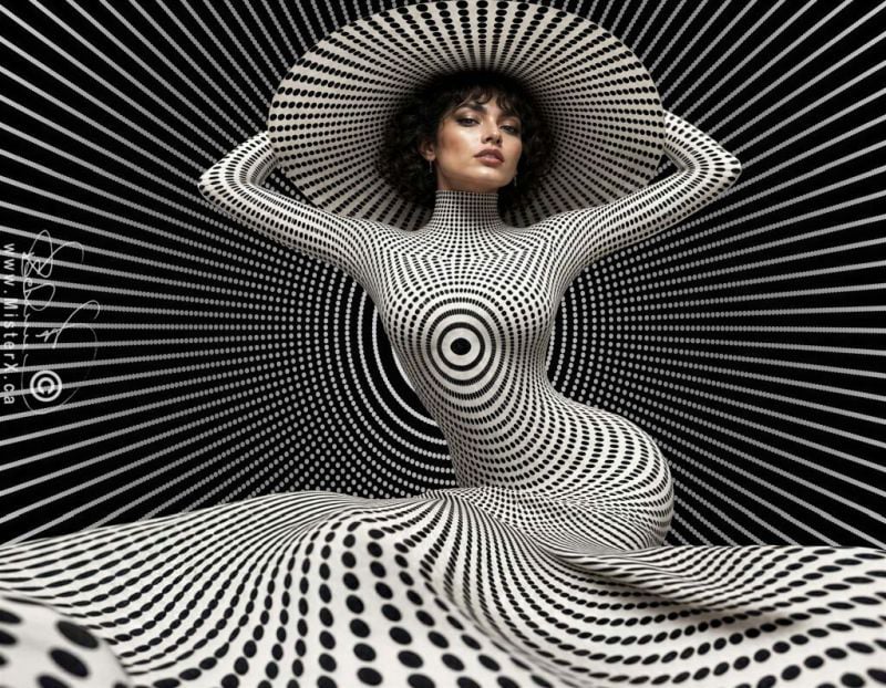 This striking photograph features a woman posing dynamically against an intricate optical illusion background that blends seamlessly with her attire. She wears a form-fitting, high-necked garment and a wide-brimmed hat, both covered in a dense pattern of black and white concentric dots and rings that distort to create a hypnotic, warping effect across her body. The background echoes this Op Art aesthetic, with radial black lines stretching outward like sunburst rays from behind her, intersected by faint dotted concentric circles that enhance the dizzying sense of depth. Holding the sides of her large hat with both hands, her dark, curly hair frames a face looking directly forward with a calm, poised expression. The bottom foreground transitions into an abstracted, undulating wave of the same black and white dotted pattern.